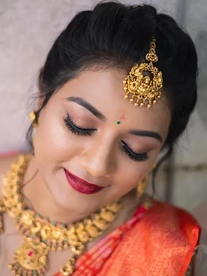A stunning bridal portrait in a vibrant orange silk saree. This look features classic winged eyeliner and a bold red lip, paired with heavy temple jewellery for a truly traditional South Indian wedding style.