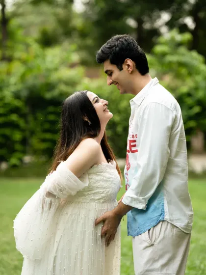 A happy and bright outdoor couple's portrait. Their joyful interaction and the fresh green surroundings make for a perfect, natural maternity photo.