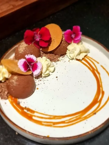 A beautifully plated chocolate dessert with edible flowers and a caramel swirl. Our expertise extends across cuisines, including decadent European-style desserts.