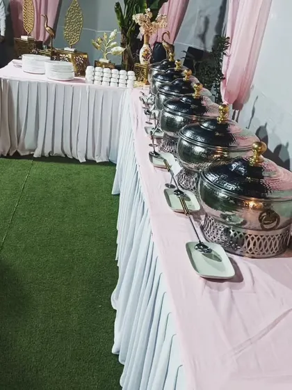 A side view of the buffet line, showing the hammered steel chafing dishes and coordinated pink and white table skirting.