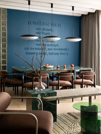 The dining area of 'ARAH' harmoniously integrates with the living space. The 16-foot sofa, green marble table, and a discreetly incorporated Jain mantra create an inviting atmosphere for family gatherings.