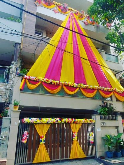 A simple yet elegant house front decoration using yellow and pink drapes to create a festive tent-like structure.
