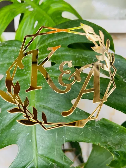 The "K&A" initial topper held against a natural green background, showing its beautiful gold reflection.