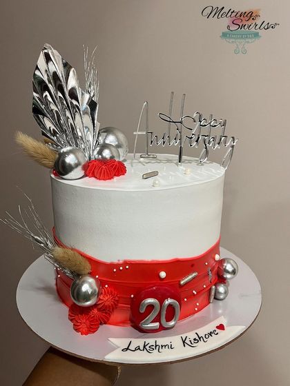 A gorgeous anniversary cake in red and white. This whipped cream cake is decorated with silver palm spears, spheres, and other elegant accents.