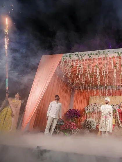 A dramatic Varmala ceremony on a stage filled with smoke and pyrotechnics. This wide shot captures the scale and theatricality of the moment, showcasing my expertise in documenting large, elaborately planned wedding events.