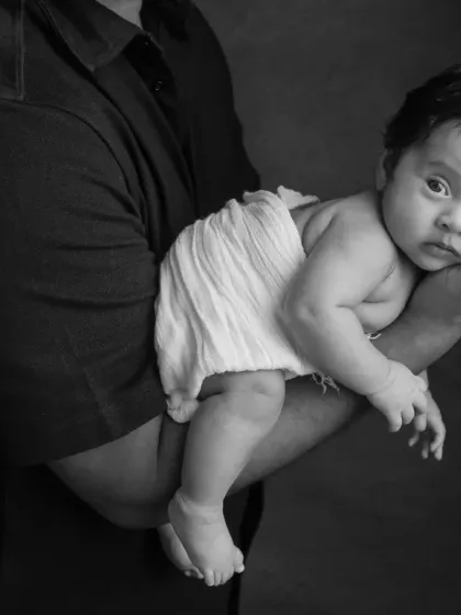 A close-up black and white shot emphasizing how small and precious the newborn is in her father's arms.