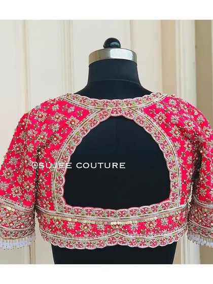 The back of the bright pink floral blouse. It features a wide keyhole cutout, with the edges and the entire blouse surface covered in dense zardozi and sequin embroidery.