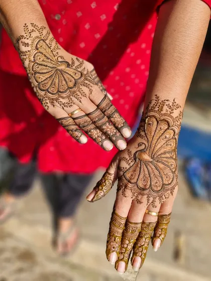 A custom design featuring a single, elegant peacock with its feathers spread across the back of the hand. The other hand has a complementary fan-like pattern.