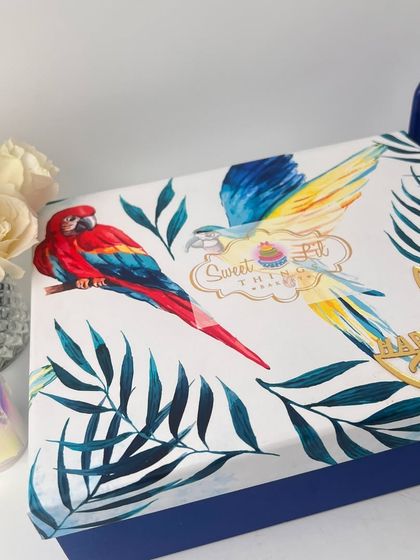 A top-down view of another one of our elegant Diwali hamper boxes. The artistic design featuring colorful parrots and tropical leaves makes it a memorable gift for the festival of lights.