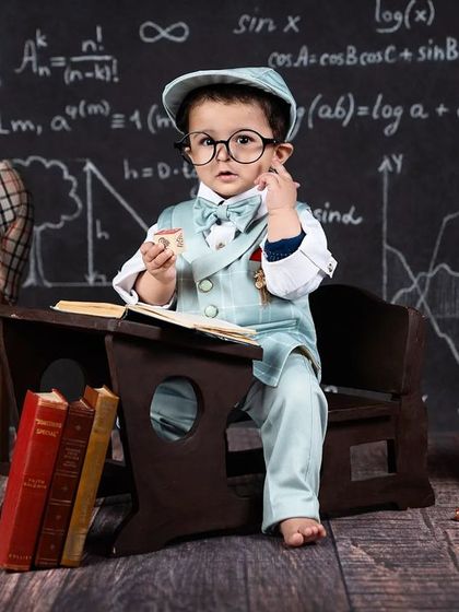 A little scholar in the making! A baby boy in a suit and glasses sits at a tiny desk, ready to learn.