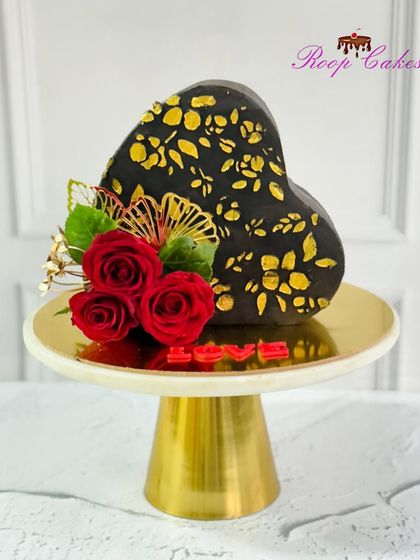 Made with love, served with a slice of sweetness. This unique top-forward heart-shaped cake features a black and gold stencil design and is adorned with red roses.