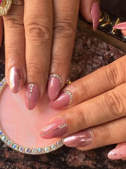 Mastering different finishes is key. Here you can see a dusty rose color with chrome effect, fine line work, and carefully placed rhinestones at the cuticle.