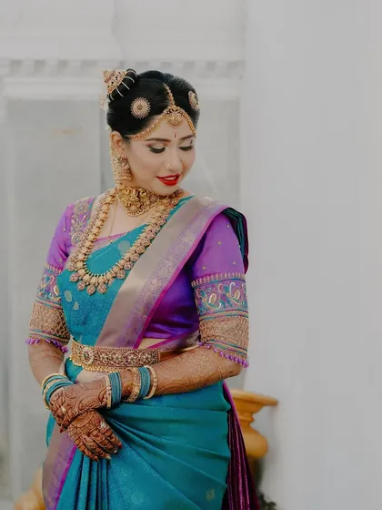 A beautiful portrait of the bride in her vibrant blue and purple saree, looking down with a gentle smile. This shot highlights the elegance of her attire and posture.