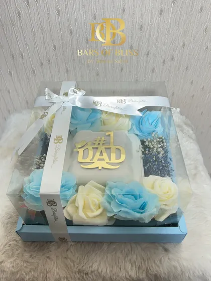 A beautiful Father's Day floral hamper with a "#1 Dad" plaque surrounded by blue and white roses, all in a clear gift box.