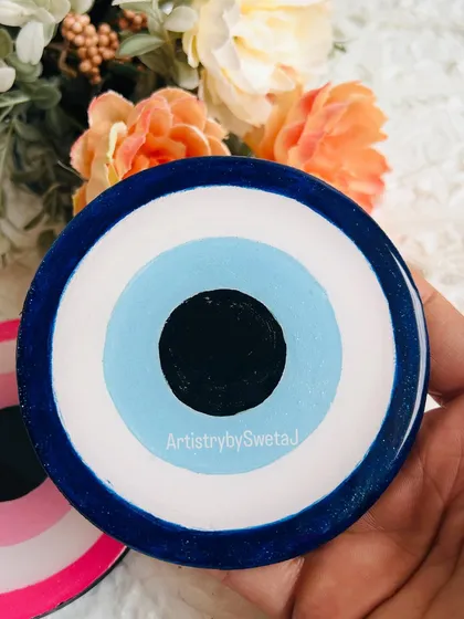 Holding the classic blue evil eye coaster. The layers of color are hand-poured to create the iconic design.