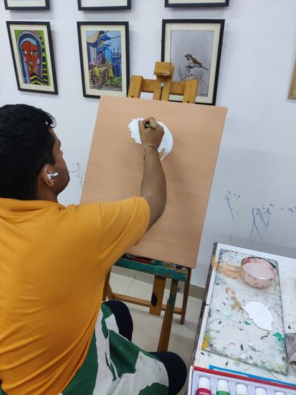 An adult student is captured through the process of painting a portrait of Sai Baba, showing concentration and devotion in his work.