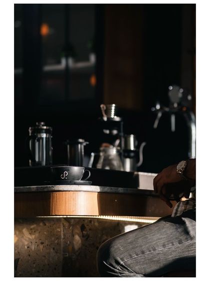 A moody shot from inside a cafe, focusing on a coffee cup on the counter. The deep shadows and highlights create a cinematic and atmospheric scene.