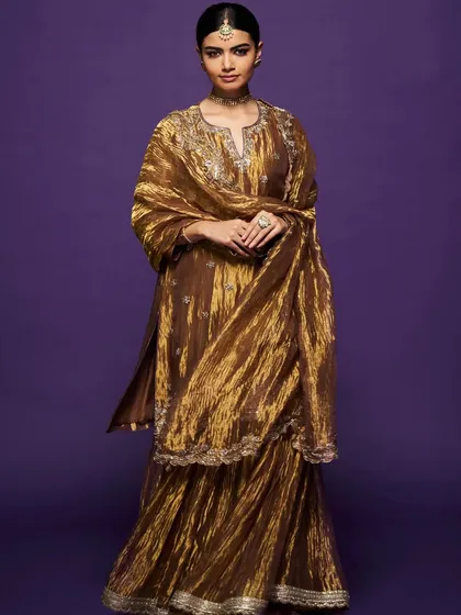 A full-length view of the metallic gold sharara set, showing its beautiful texture and the way it catches the light.