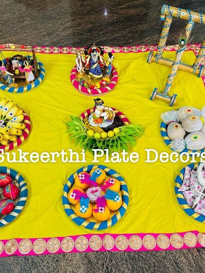 This colorful baby shower setup on a yellow cloth includes a miniature walker and cradle. The peacock feather design on the bananas is a small detail that makes a big impact.