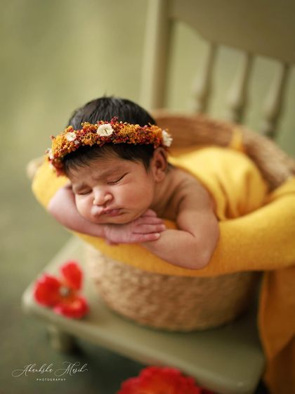 This sweet baby girl, just nine days new, looks so peaceful in this basket setup. The warm yellow wrap and delicate floral crown add a touch of earthy elegance to her newborn portrait.
