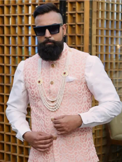 A confident look in a light peach brocade waistcoat, layered on a pristine white kurta and accessorized with a pearl necklace. This is modern classic style for a wedding.