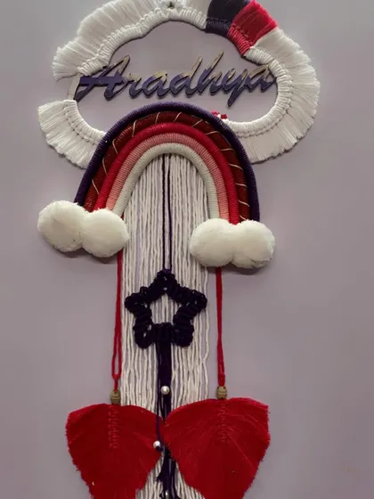 A full, clear shot of the finished 'Aradhya' nameplate. The design features a color-blocked cloud, a warm-toned rainbow, a star, and two red macrame leaves.