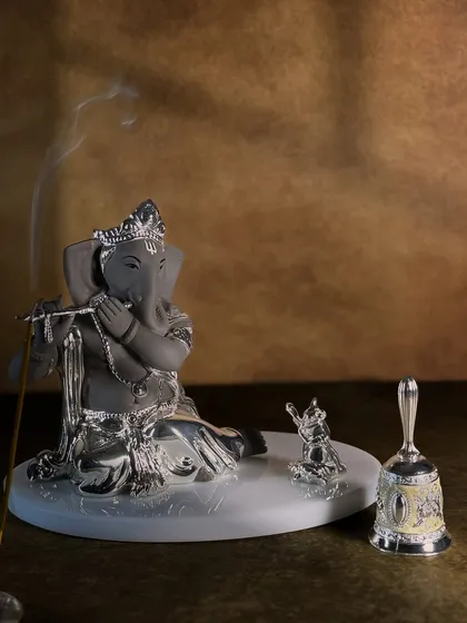 The tranquil presence of Lord Ganesha playing the flute, accompanied by his divine vehicle, the mouse. The gentle wisp of incense smoke adds to the serene and meditative atmosphere this idol creates.