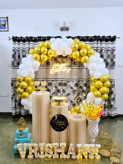 A white and gold balloon arch set up in a home against curtains. The neon sign and light-up name create a beautiful and celebratory focal point.