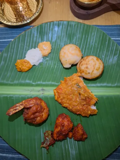 A platter of delicious South Indian appetizers, including fried prawns and paniyaram, served on a banana leaf.