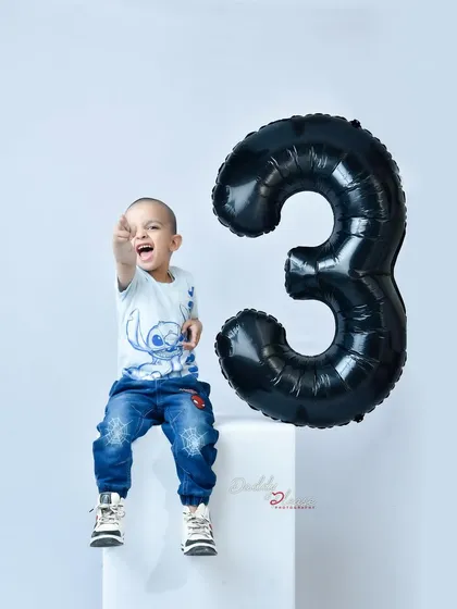 A fun and energetic shot of a three year old birthday boy pointing excitedly at the camera. His personality shines through in this playful studio portrait.