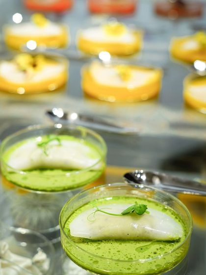 Translucent raviolis served in petri dishes, part of an artistic food presentation. The green and yellow fillings were designed to emulate the colors of the fashion collection being launched.