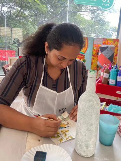 A participant carefully applies a design to a bottle during a decoupage workshop. The focus required is part of the therapeutic experience.