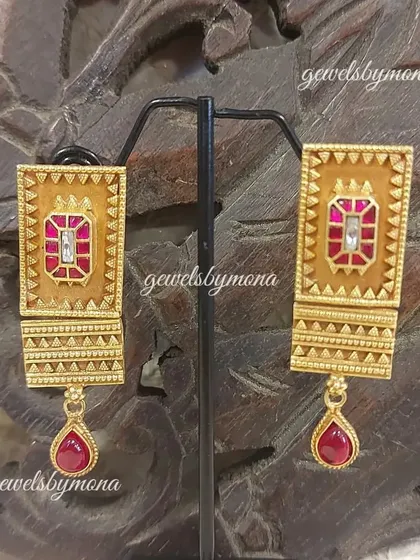 These rectangular Dakshinaya earrings feature a ruby-colored stone set in detailed gold work with a matching drop. The design is inspired by the architectural elements of South Indian temples.