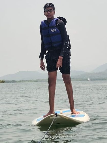 A camper practices his balance on a stand-up paddleboard (SUP) for the first time in the calm waters of Karwar.