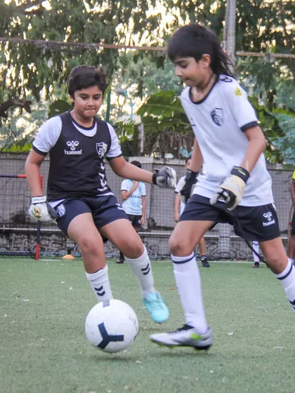 Two players, including a goalkeeper playing out, compete for the ball, highlighting the importance of footwork for every position.