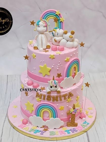A magical two-tier unicorn cake for a first birthday. This chocolate and butterscotch cake is decorated in a lovely pink with rainbows, stars, and cute fondant unicorns.