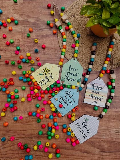 We love working with colorful wooden beads, and these beaded wooden hut hangings are a great example. This image shows a variety of designs, each with a unique quote and vibrant beads.