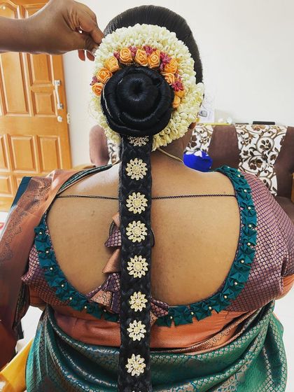 A detailed look at a traditional baby shower hairstyle, featuring a neat bun and an elaborate floral and accessory arrangement on the braid.