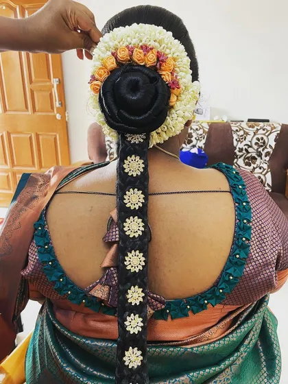 A detailed look at a traditional baby shower hairstyle, featuring a neat bun and an elaborate floral and accessory arrangement on the braid.