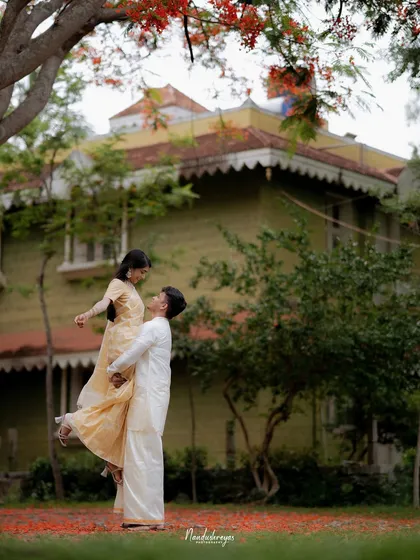 A joyful lift, with the groom lifting his bride-to-be in front of a traditional house with red flowers scattered on the ground.