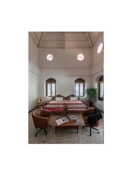 A sitting area featuring a mix of inherited and modern furniture. The high ceilings with circular windows, a unique feature of the building, have been restored to fill the space with natural light.