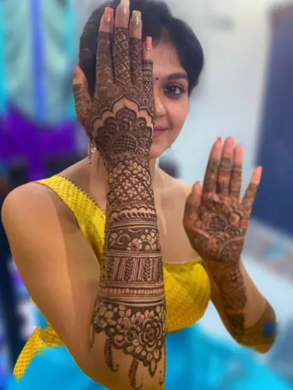 A happy client showing off her full-arm bridal mehendi, with one arm complete and the other showing a simpler design on the palm.