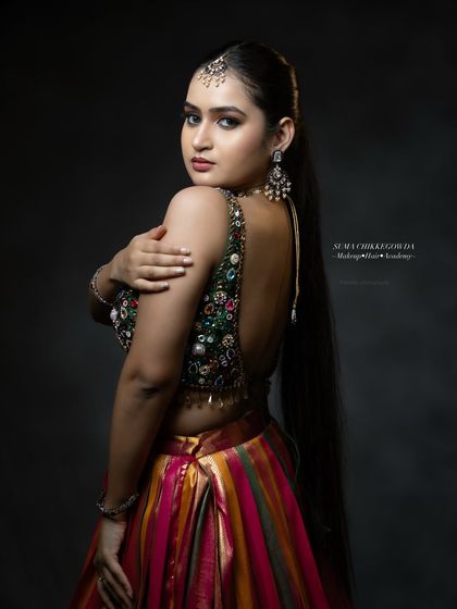 A stunning look for a Sangeet or reception, featuring a heavily embellished blouse and a multi-colored lehenga. The makeup is kept glamorous with a focus on defined eyes and contoured features.