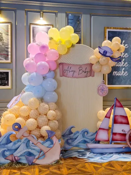 A complete "Ahoy, Baby!" nautical-themed birthday setup. The decor features a sailboat, anchor, ship's wheel, and a pastel balloon garland, perfect for a little sailor's first birthday.