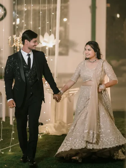 Amit and Pallavi walk hand-in-hand, smiling, through a path lit by fairy lights, capturing the magic of their engagement night.