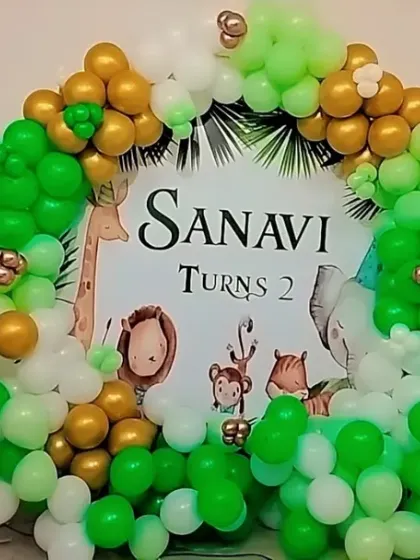 A jungle-themed second birthday with a custom backdrop and a green and gold balloon ring.