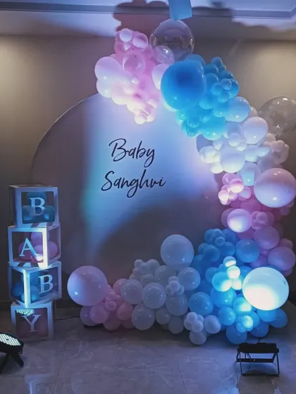 A creative gender reveal decoration using pink and blue lighting on a white balloon arch. This setup, with 'BABY' blocks and a simple backdrop, keeps the surprise until the final color is revealed.