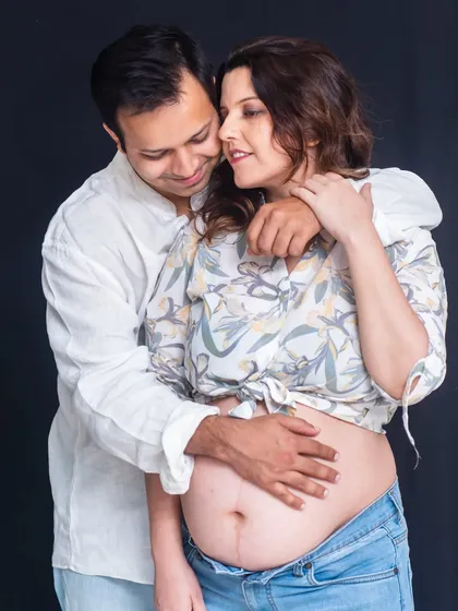 A casual and intimate studio shot. The couple embraces, showing off the bare baby bump in a relaxed and natural way.