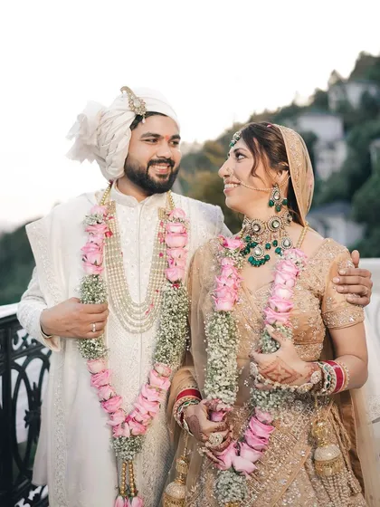 A happy portrait of the couple, adorned with beautiful floral garlands, sharing a look of love on a balcony overlooking the mountains.