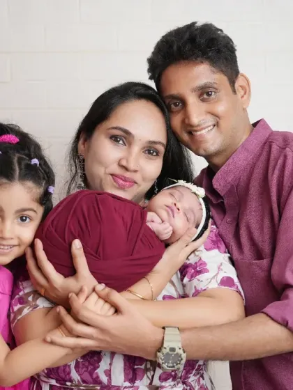 A beautiful portrait of a family of four, celebrating the arrival of their newborn. The older sister looks on as her parents hold the new baby, capturing a special milestone.
